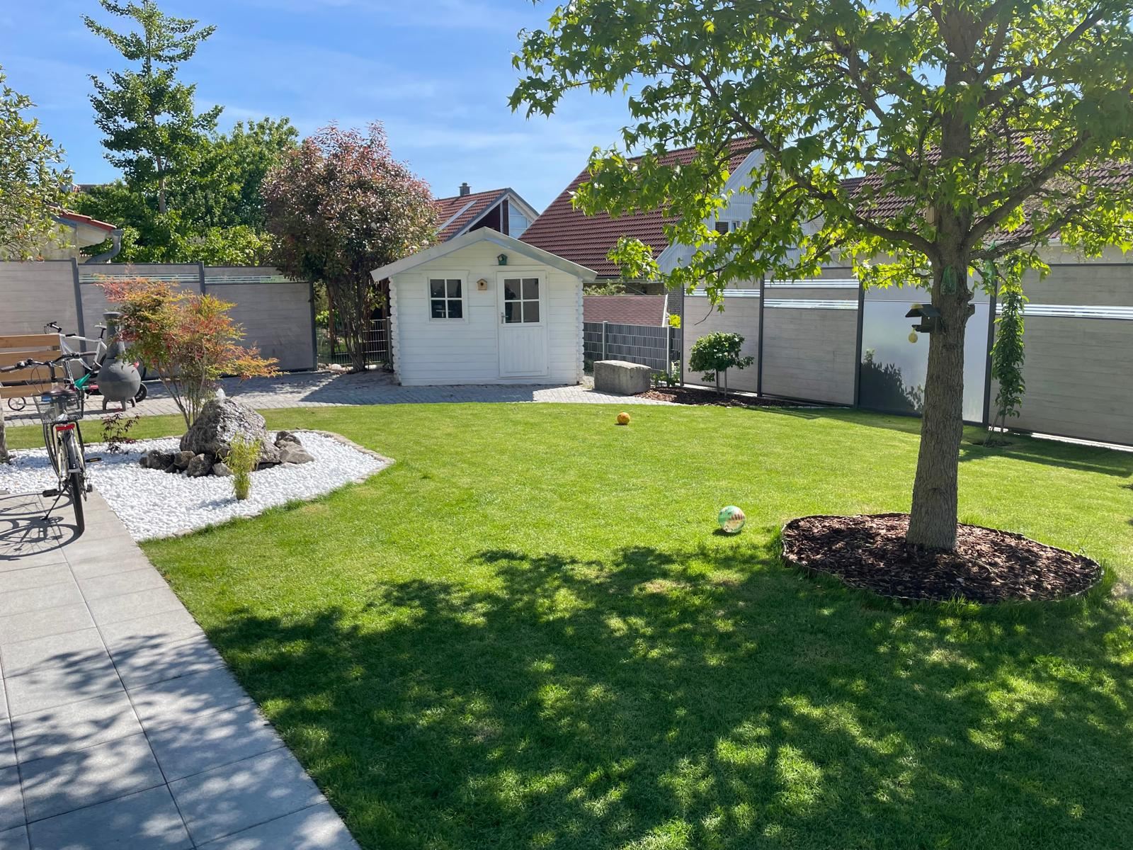 Gepflegter Privatgarten mit Rasenfläche, Kiesbeet, Ahorn und Gartenhaus.