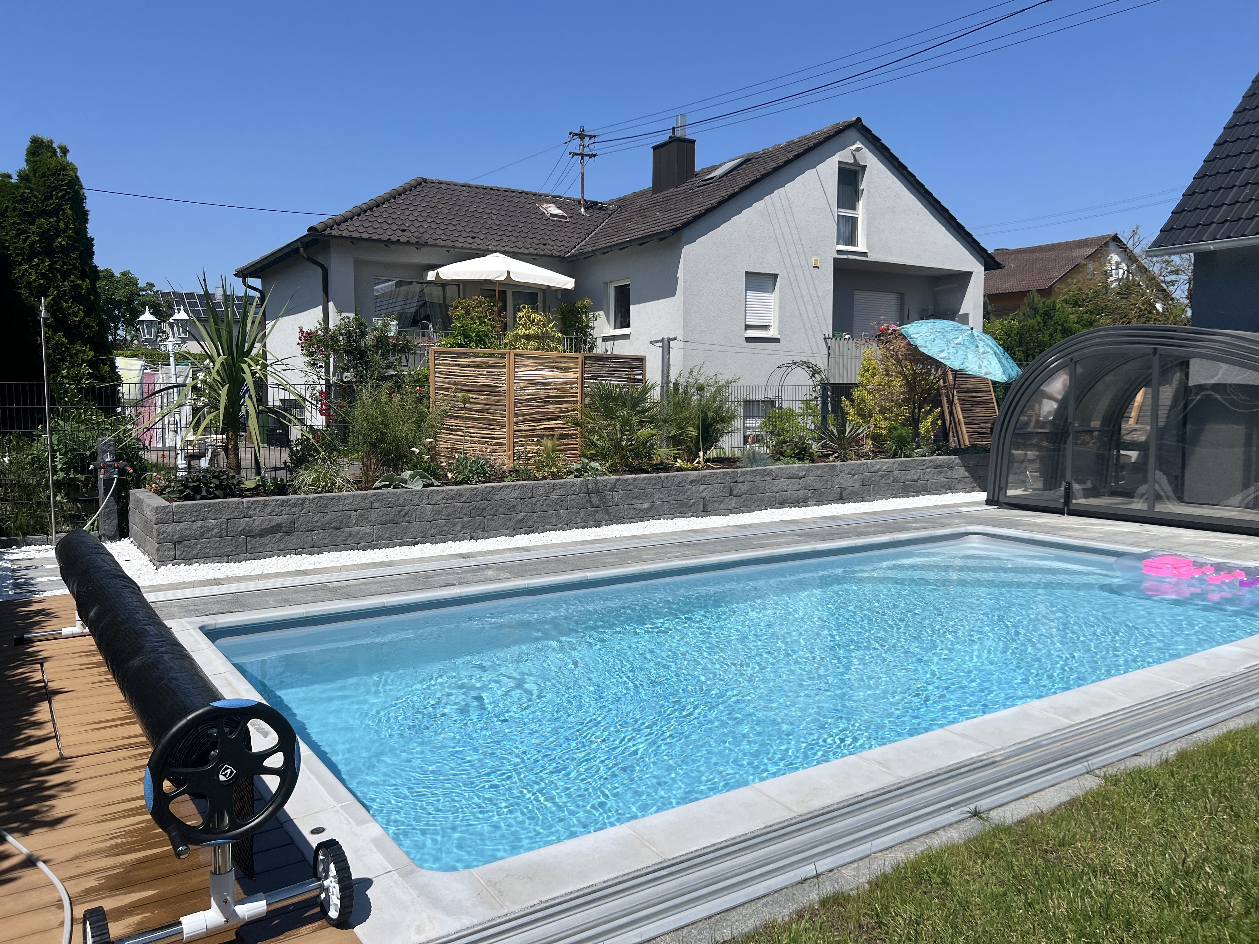 Pool, Plattenterrasse und Hochbeet aus grauen Schichtsteinen mit Stauden und Ahorn.